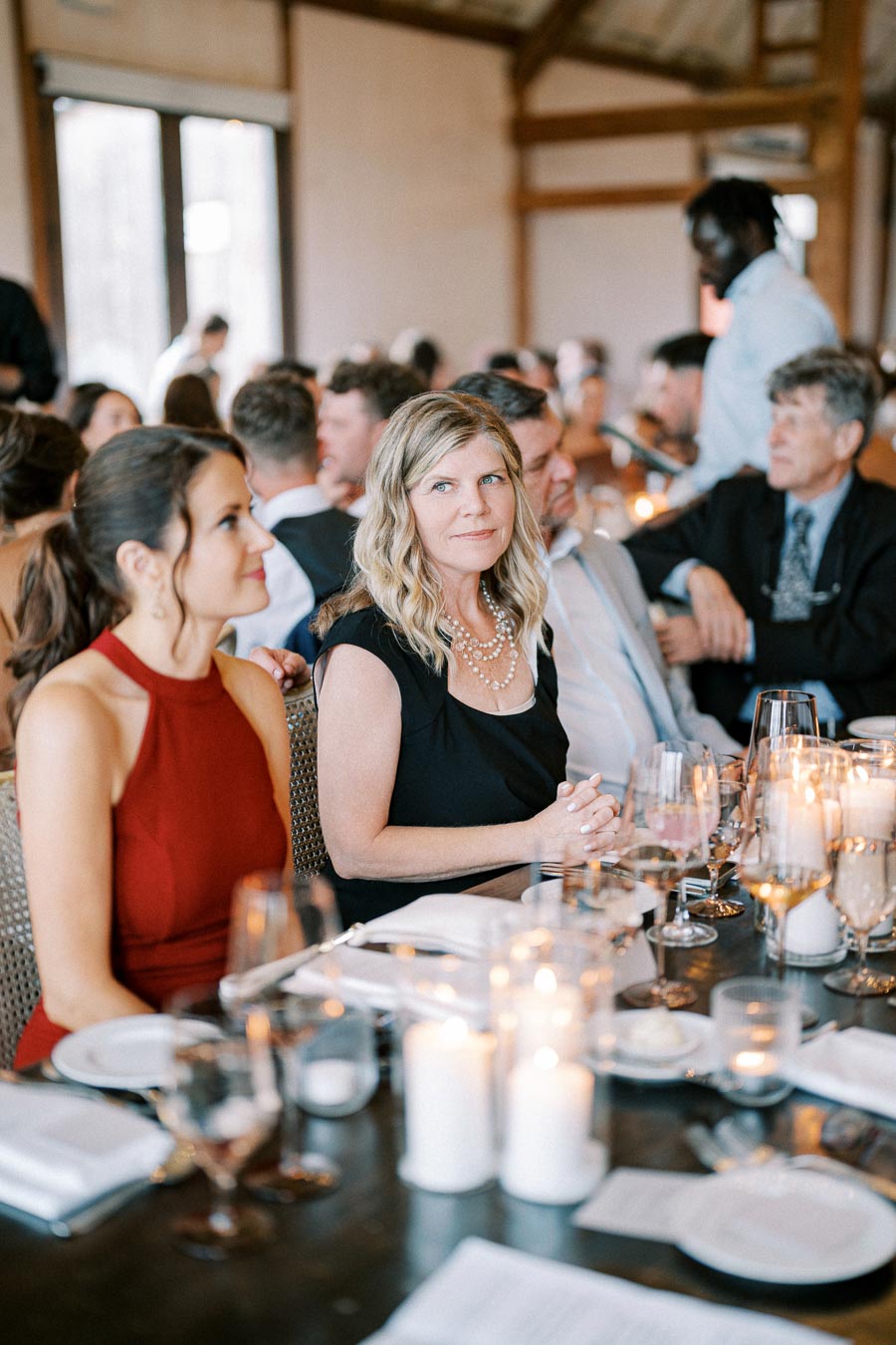 Elegant indoor event with guests seated at a beautifully decorated table adorned with candles and glassware, creating a warm and inviting atmosphere.