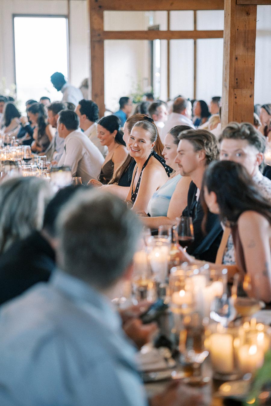 A diverse group of guests seated at a long, elegantly decorated dining table during a lively event, with candles and glasses creating a warm and inviting atmosphere.