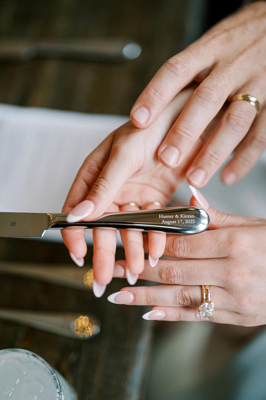 Close-up of hands holding an engraved wedding cake knife with the date August 17, 2025, symbolizing marriage celebration.