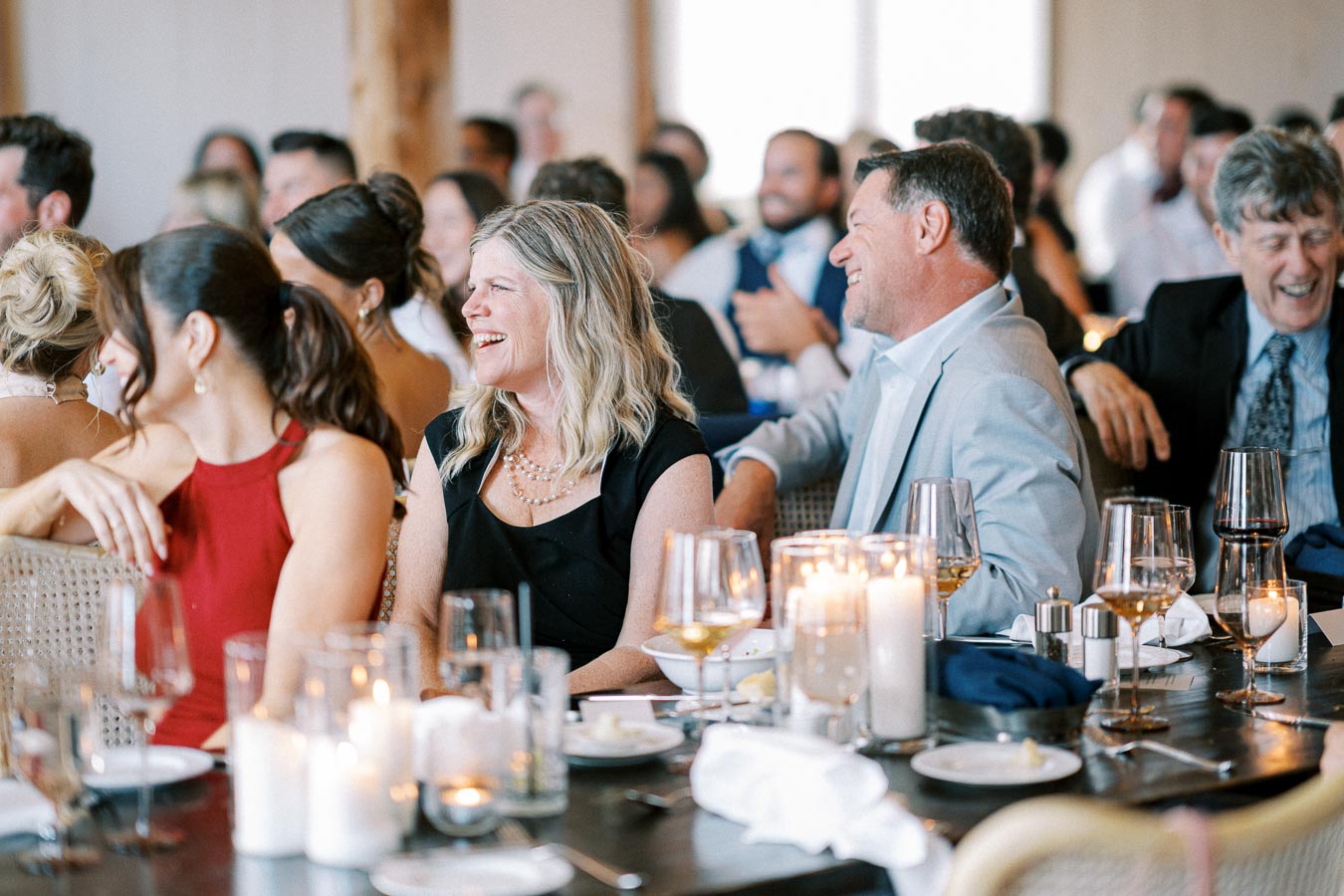 A group of people smiling and enjoying a dinner event, with beautifully set tables, candles, and wine glasses, creating a warm and joyful atmosphere.