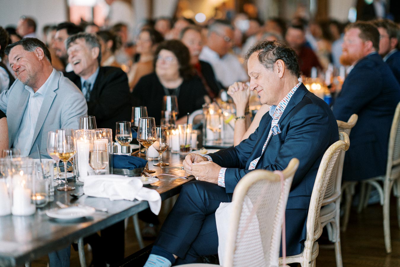 Elegant dinner event with well-dressed guests at a long table, featuring candlelit ambiance and decorative glassware.