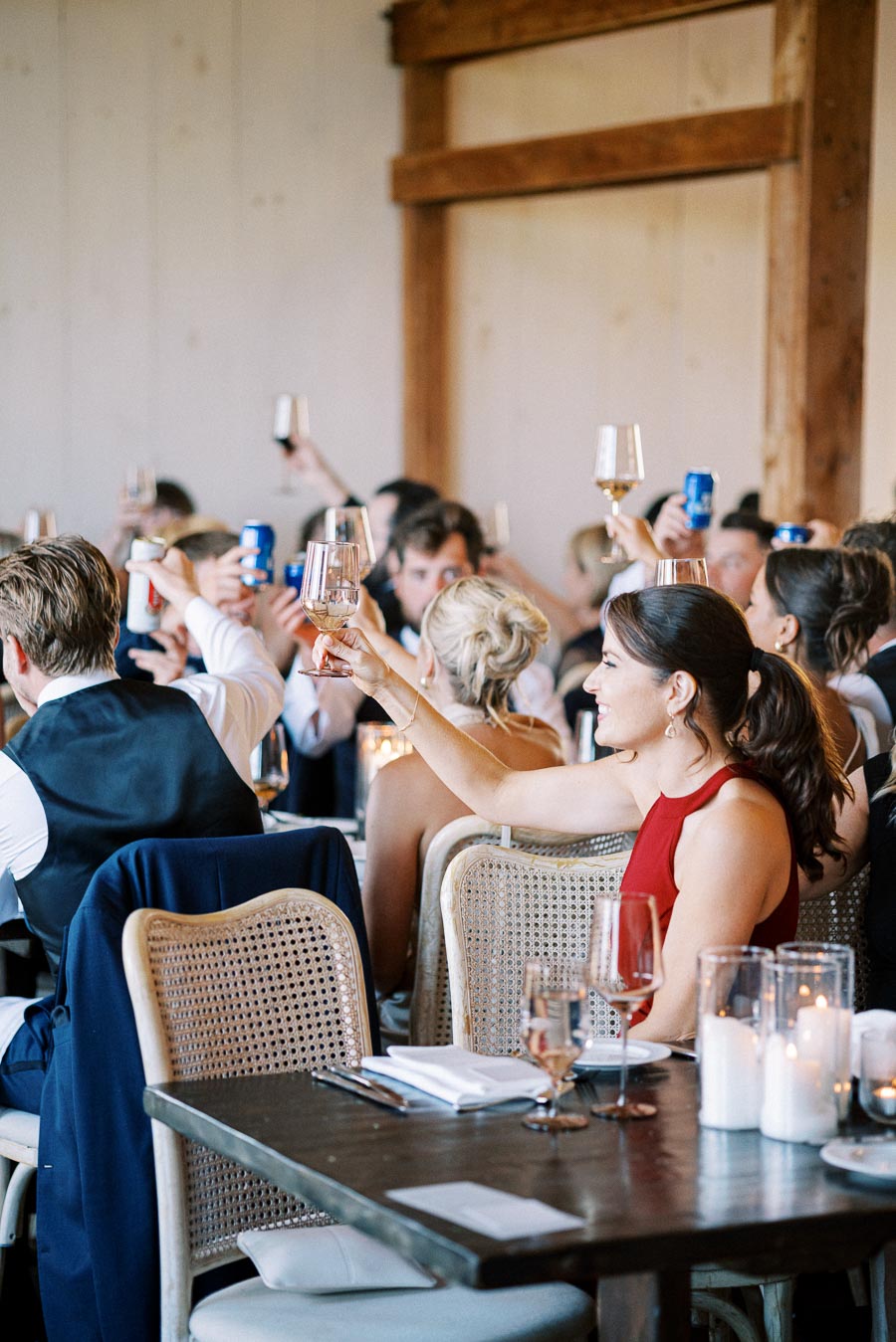 People raising glasses in a celebratory toast at an indoor event, featuring elegantly set tables and warm ambiance.