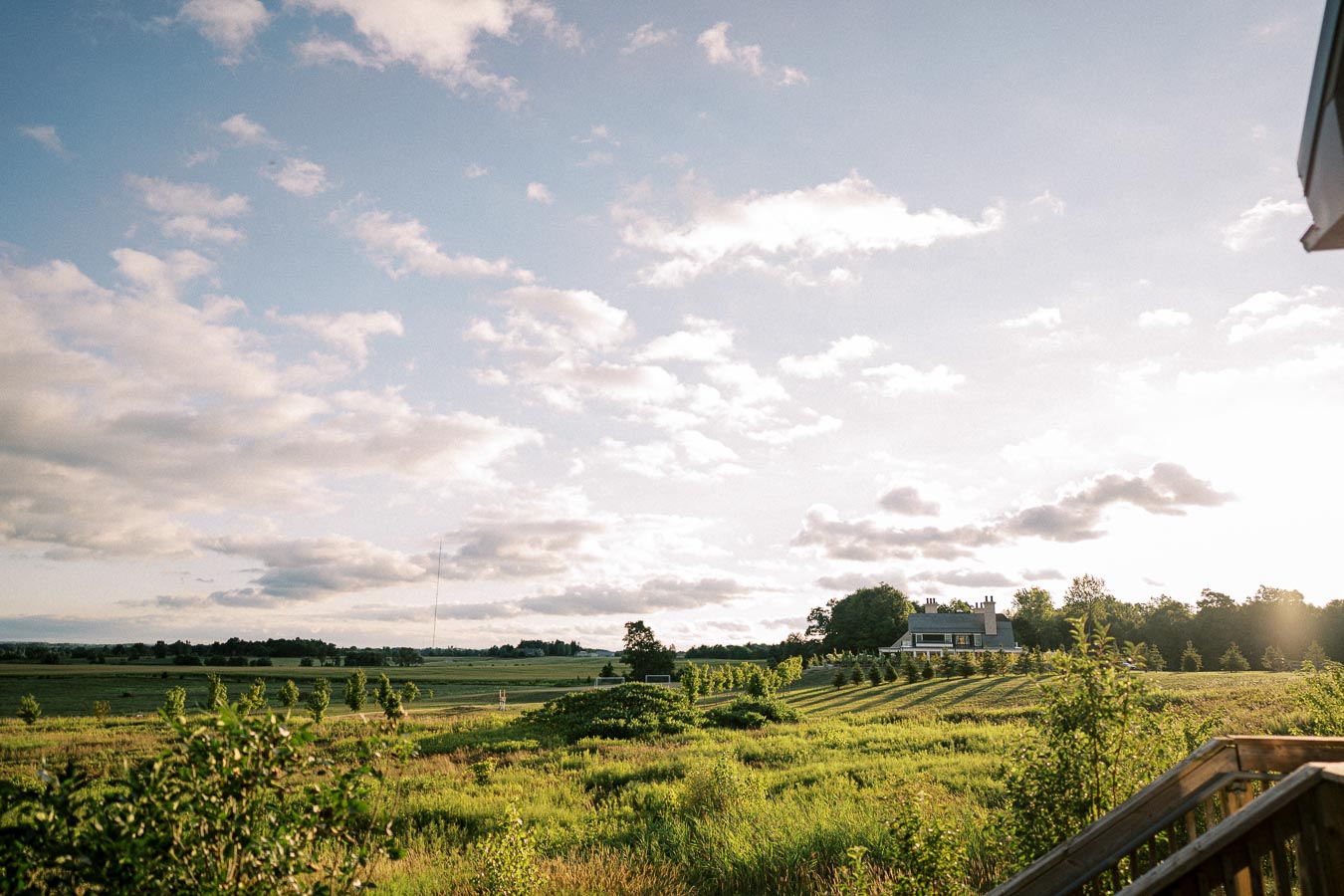 Scenic view of a picturesque countryside landscape at sunset with a sprawling field, lush greenery, and a distant house under a sky filled with fluffy clouds.