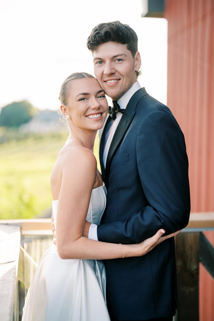 Smiling bride and groom embracing outdoors in elegant wedding attire on a sunny day