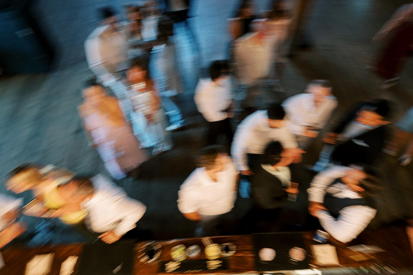 Blurred image showing a group of people mingling at an indoor event, viewed from above near a bar area.