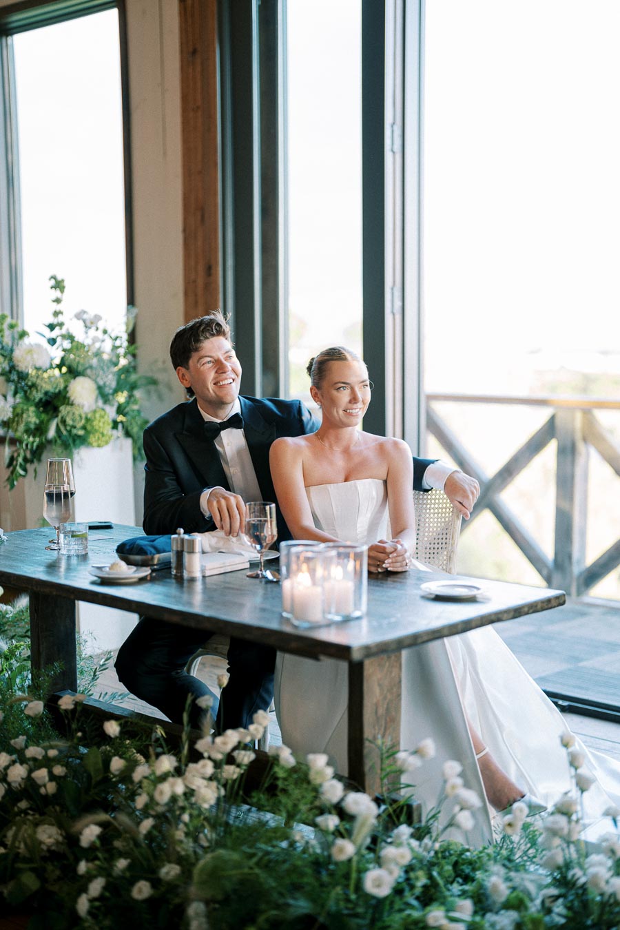 A couple enjoying their wedding reception, seated at a beautifully decorated table with flowers and candles.