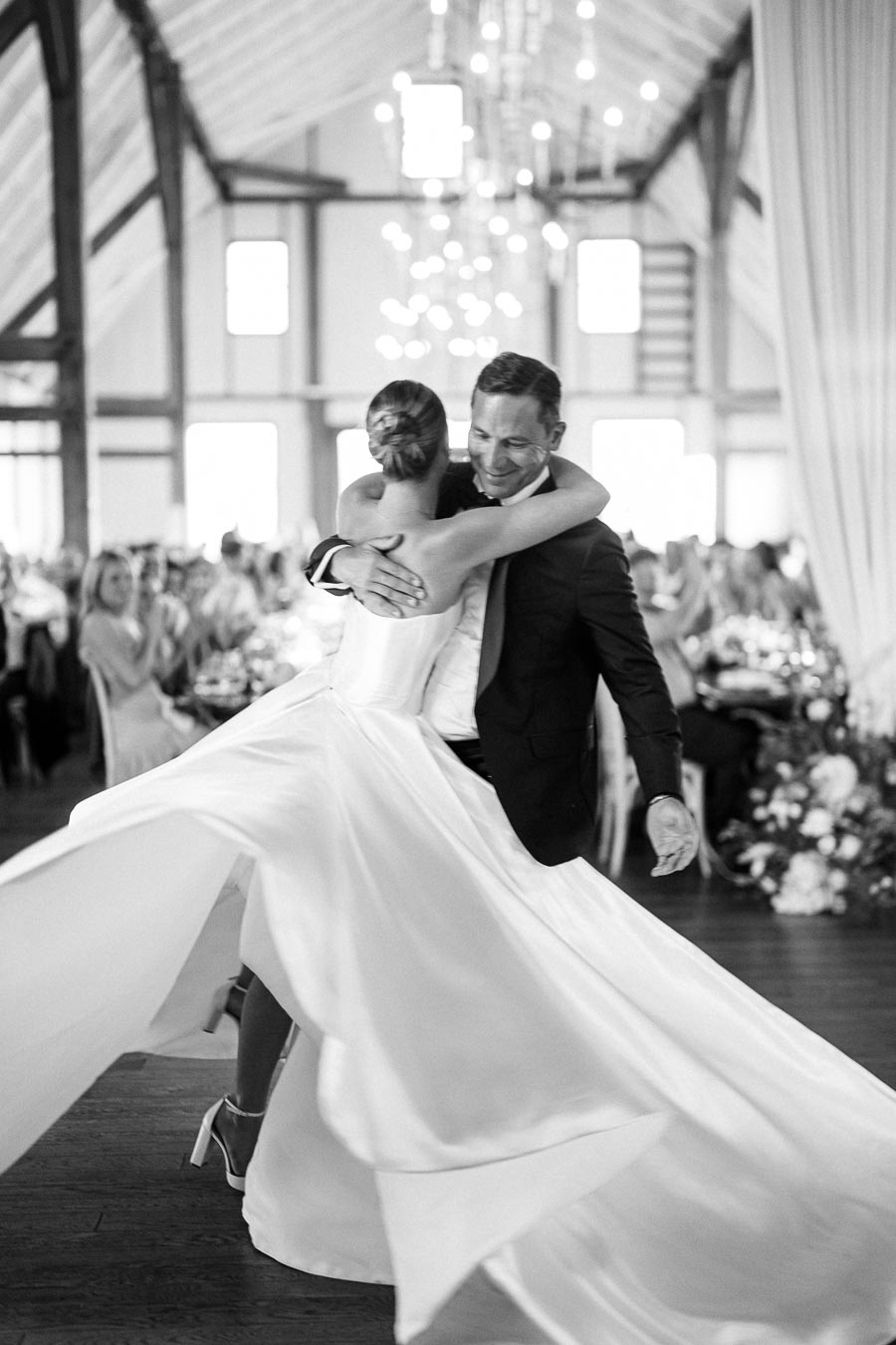 A bride and groom joyfully dance in a beautifully decorated venue, her dress flowing elegantly as they embrace, capturing a candid moment of celebration and love.