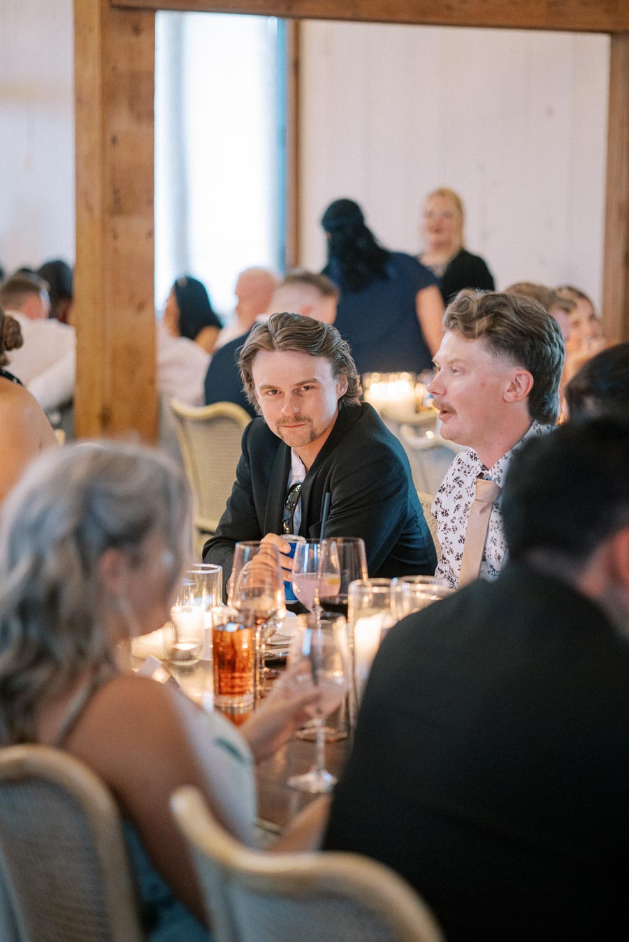 Guests sitting at a table during a wedding reception, with elegant decor and glowing candles creating a warm ambiance.