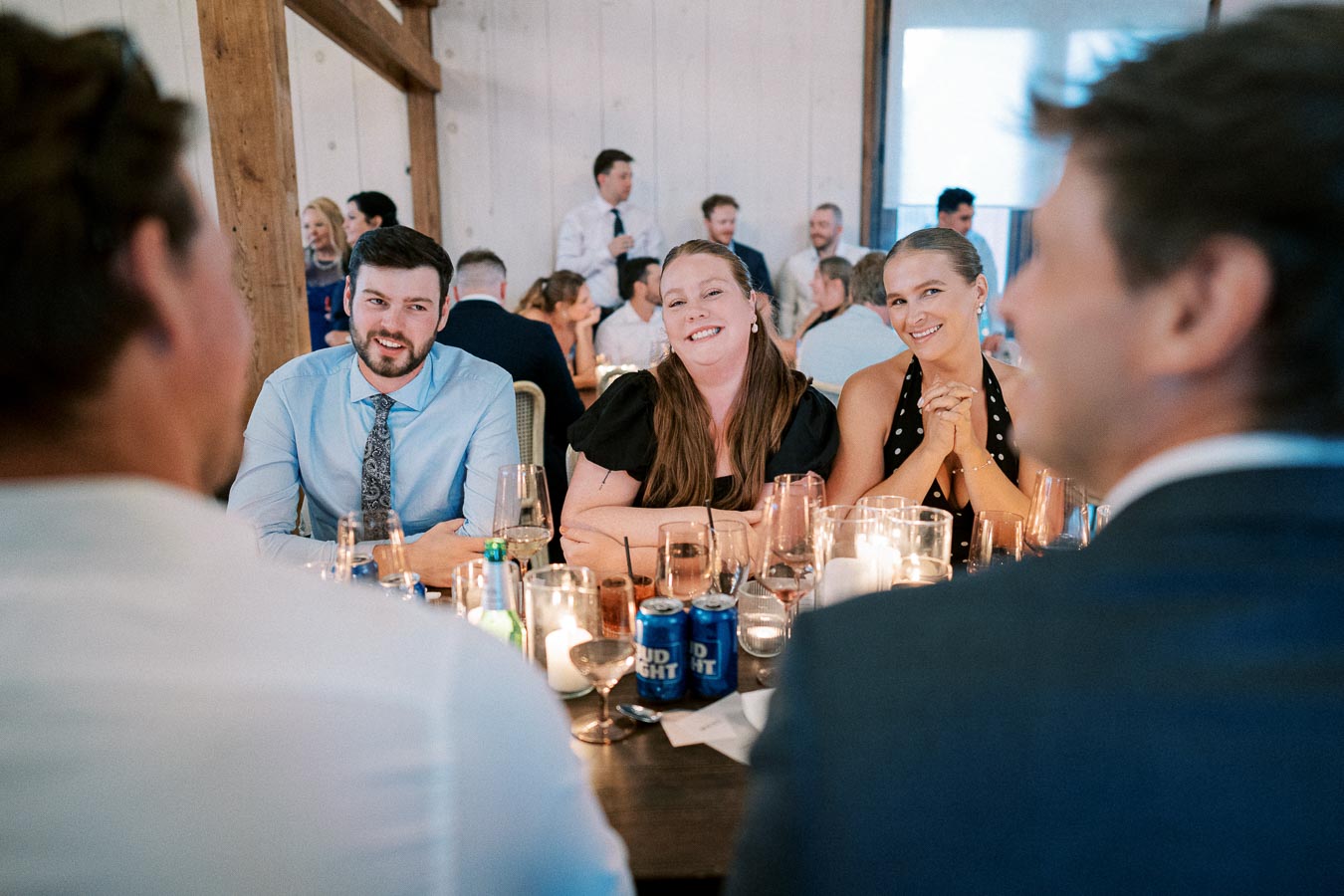 A group of people sitting at a table during a lively indoor event, engaging in conversation and surrounded by glasses and candles, creating a warm and social atmosphere.