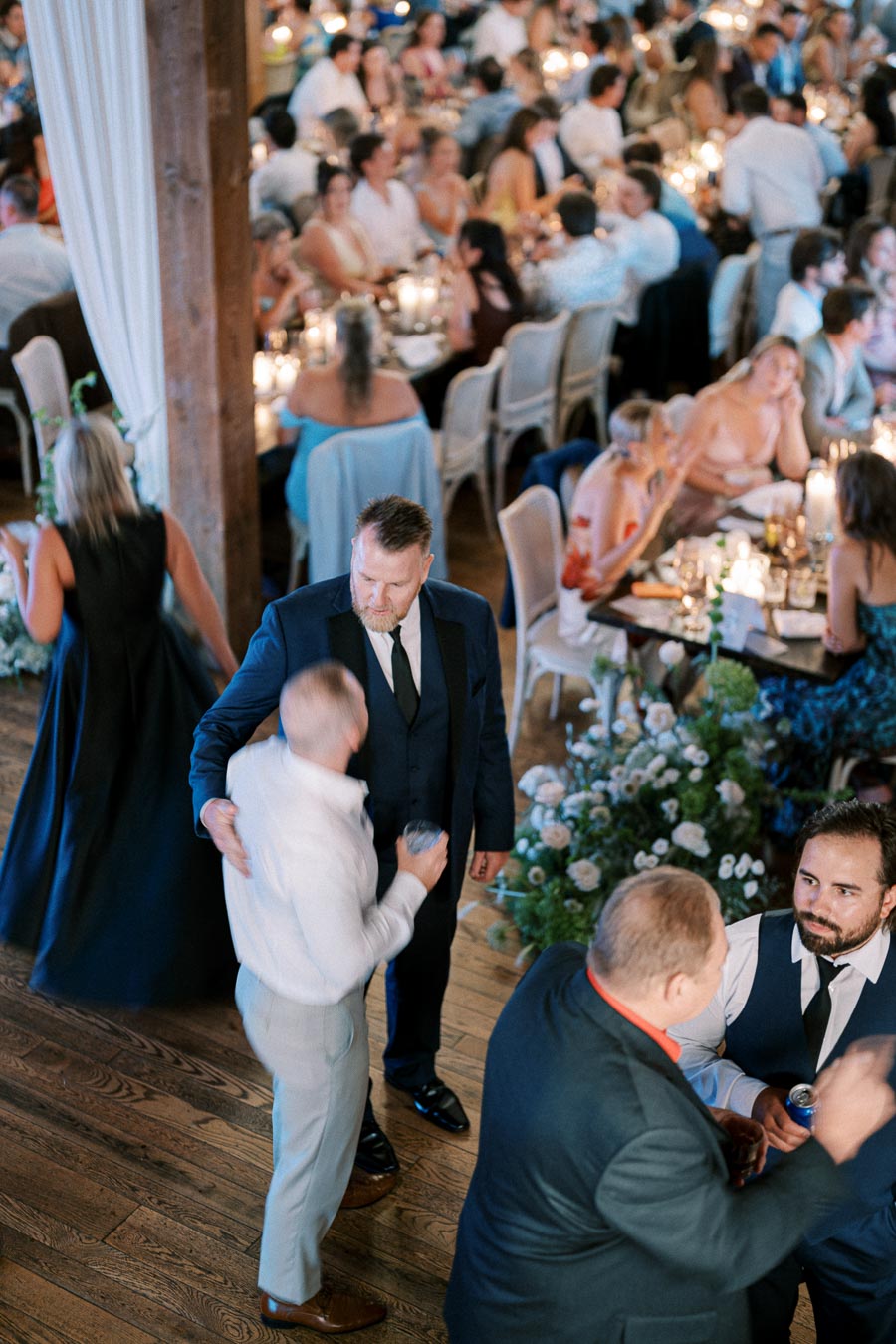 Guests socializing at a lively wedding reception with elegantly decorated tables, warm lighting, and vibrant floral arrangements.