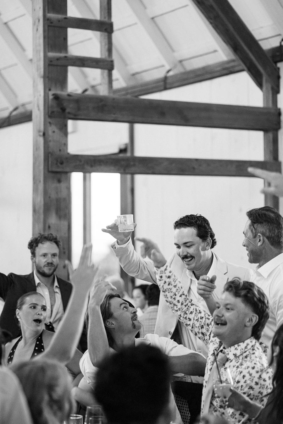 Black and white photo of a joyful group of people celebrating at a social gathering, with one person raising a glass in a toasting gesture.