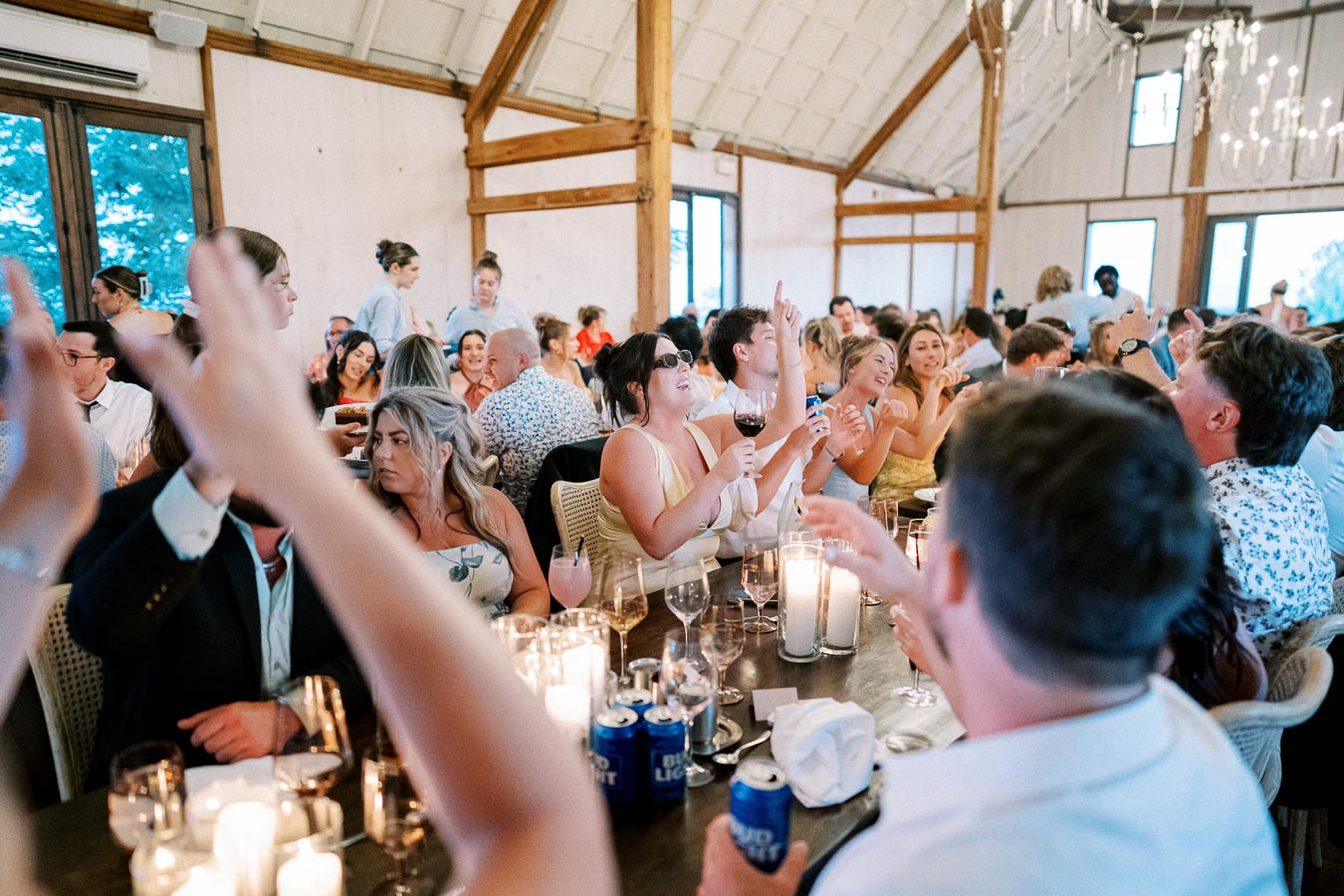 Guests enjoying a lively wedding reception inside a rustic venue, with drinks in hand and candlelit ambiance, creating a warm and festive atmosphere.