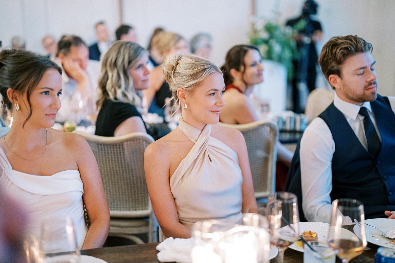 A group of elegantly dressed guests seated at a formal event, enjoying a beautifully decorated dining setting with candles and tableware.