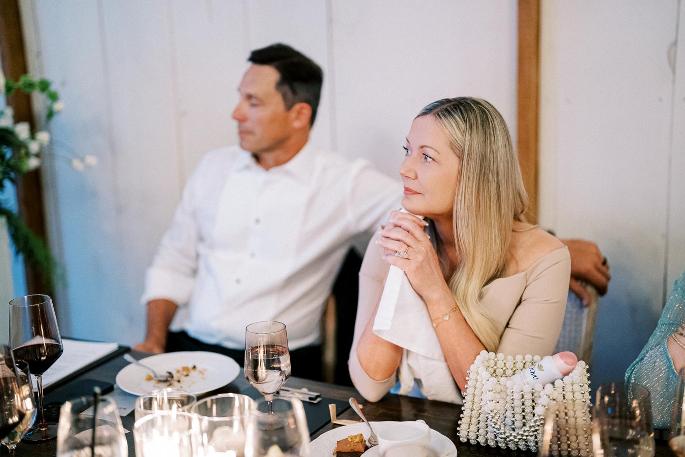 Elegant dinner gathering with a couple seated at a candlelit table, surrounded by wine glasses and plated food, highlighting a sophisticated and intimate atmosphere.