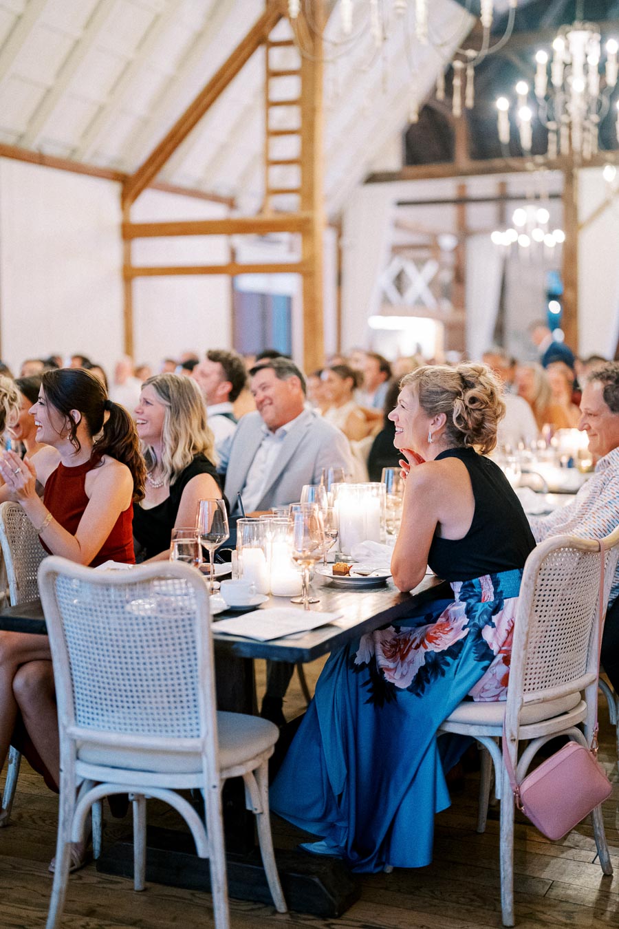 Guests enjoying a wedding reception in a beautifully decorated barn venue, featuring elegant chandeliers and candlelit tables, creating a warm and festive ambiance.