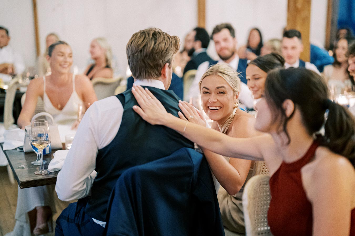A joyful wedding reception scene with guests laughing and socializing around a dinner table, highlighting friendship and celebration.