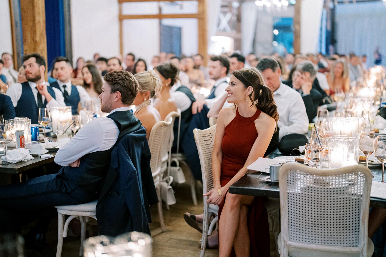 Guests attentively listening during a formal dinner event, with elegant table settings and ambient candlelight enhancing the sophisticated atmosphere.