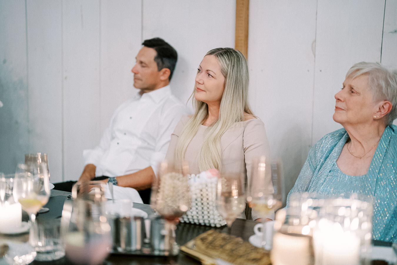 Three people sitting at a table during an elegant event, surrounded by glasses and candles.