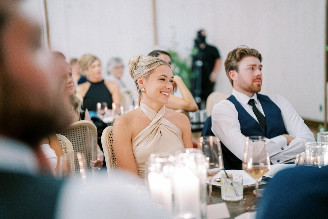Guests smiling and enjoying an elegant indoor event, dressed in formal attire, surrounded by candlelight and glasses on the table.