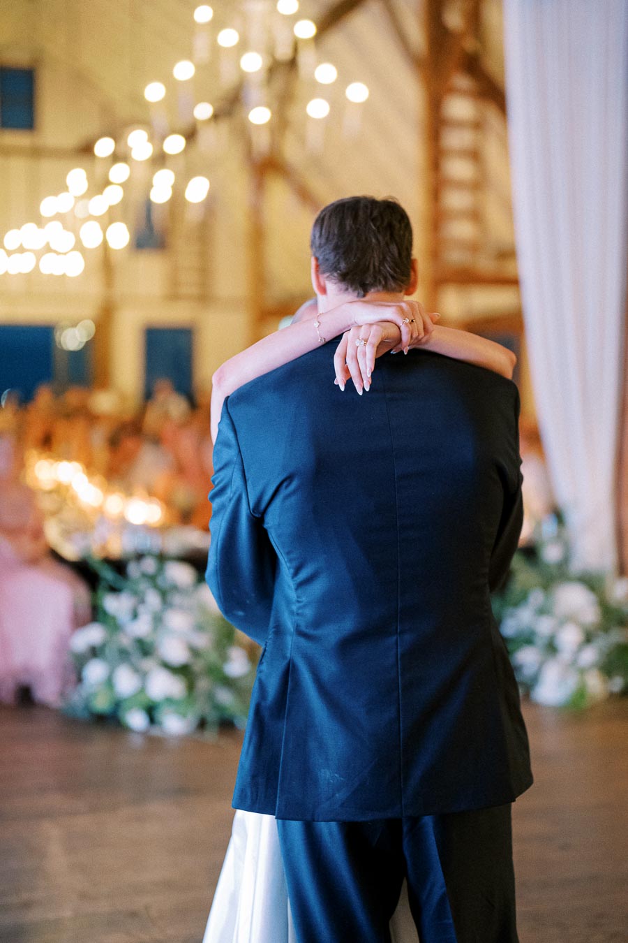 A bride and groom sharing their first dance at a beautiful wedding reception, surrounded by soft lighting and elegant décor in a rustic barn setting.