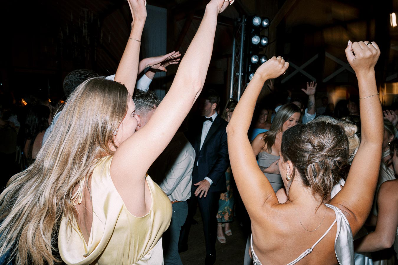 People dancing enthusiastically at a wedding reception, with women in elegant dresses and a festive atmosphere.