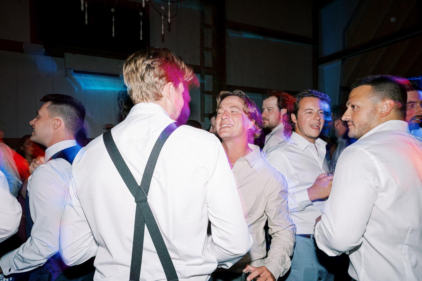 A group of men in formal attire enjoying a lively indoor party with colorful lighting effects.