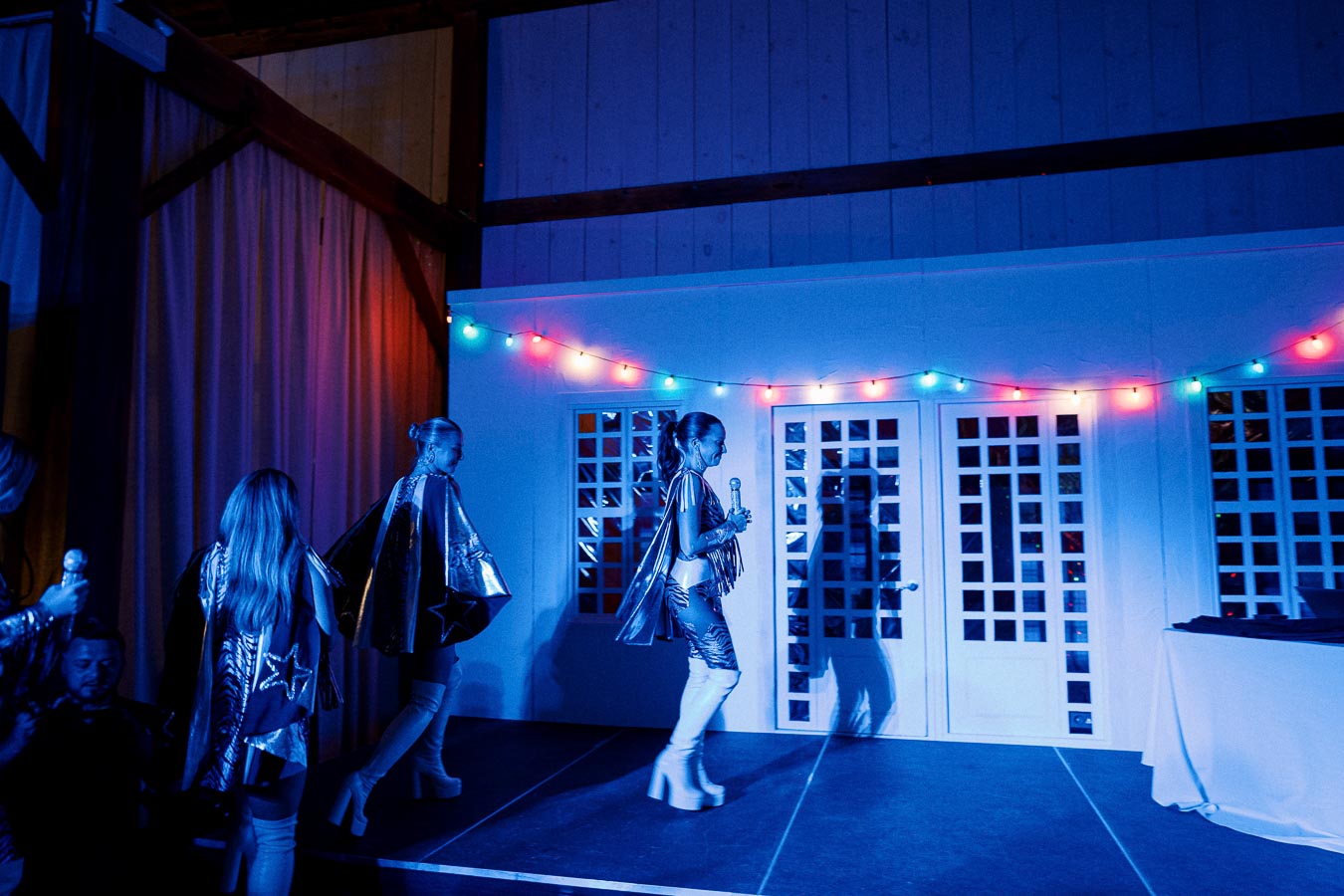 Performers in futuristic costumes walking on stage under colorful lights at an event.