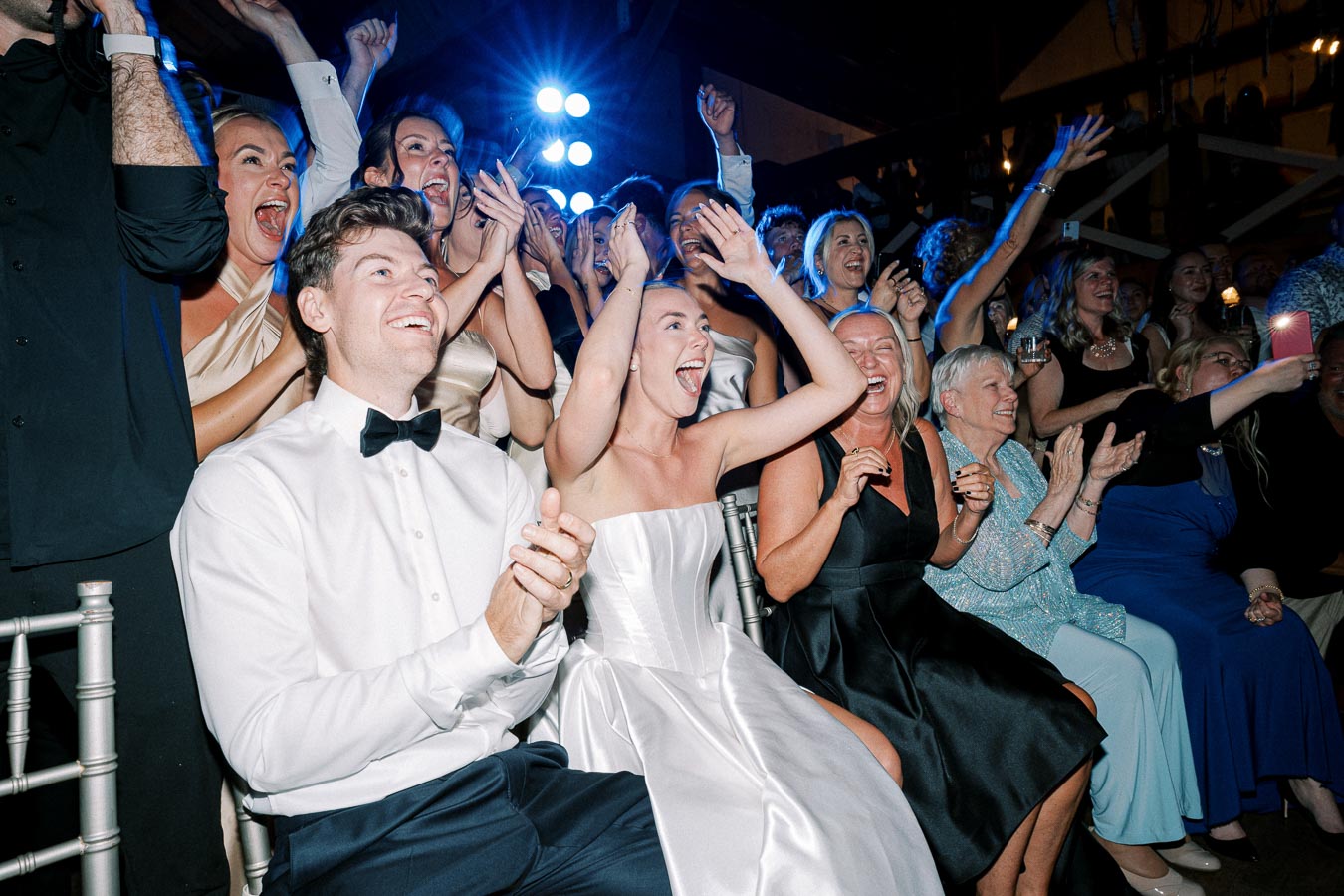 A joyous wedding celebration with guests in formal attire clapping and cheering, highlighting the vibrant atmosphere and festive mood.