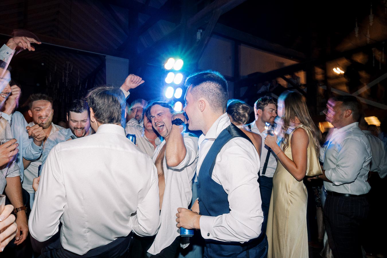 A lively group of wedding guests dancing and celebrating on a vibrant dance floor, wearing formal attire, with bright party lights in the background.