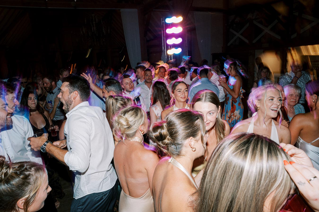 A lively wedding reception with guests dancing and socializing under colorful lights, capturing the joyful and vibrant atmosphere of the celebration.