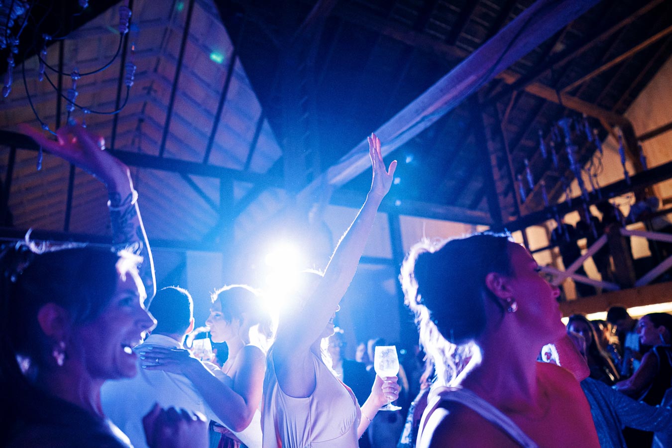 A vibrant wedding reception in a rustic barn with guests dancing and raising glasses, highlighted by colorful lighting and a festive atmosphere.