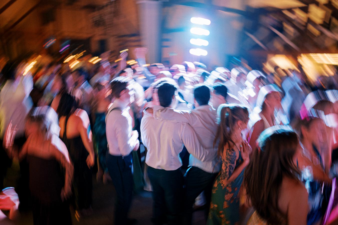 Blurry image of a lively crowd dancing at a party, with colorful lights and motion creating a vibrant, energetic atmosphere.