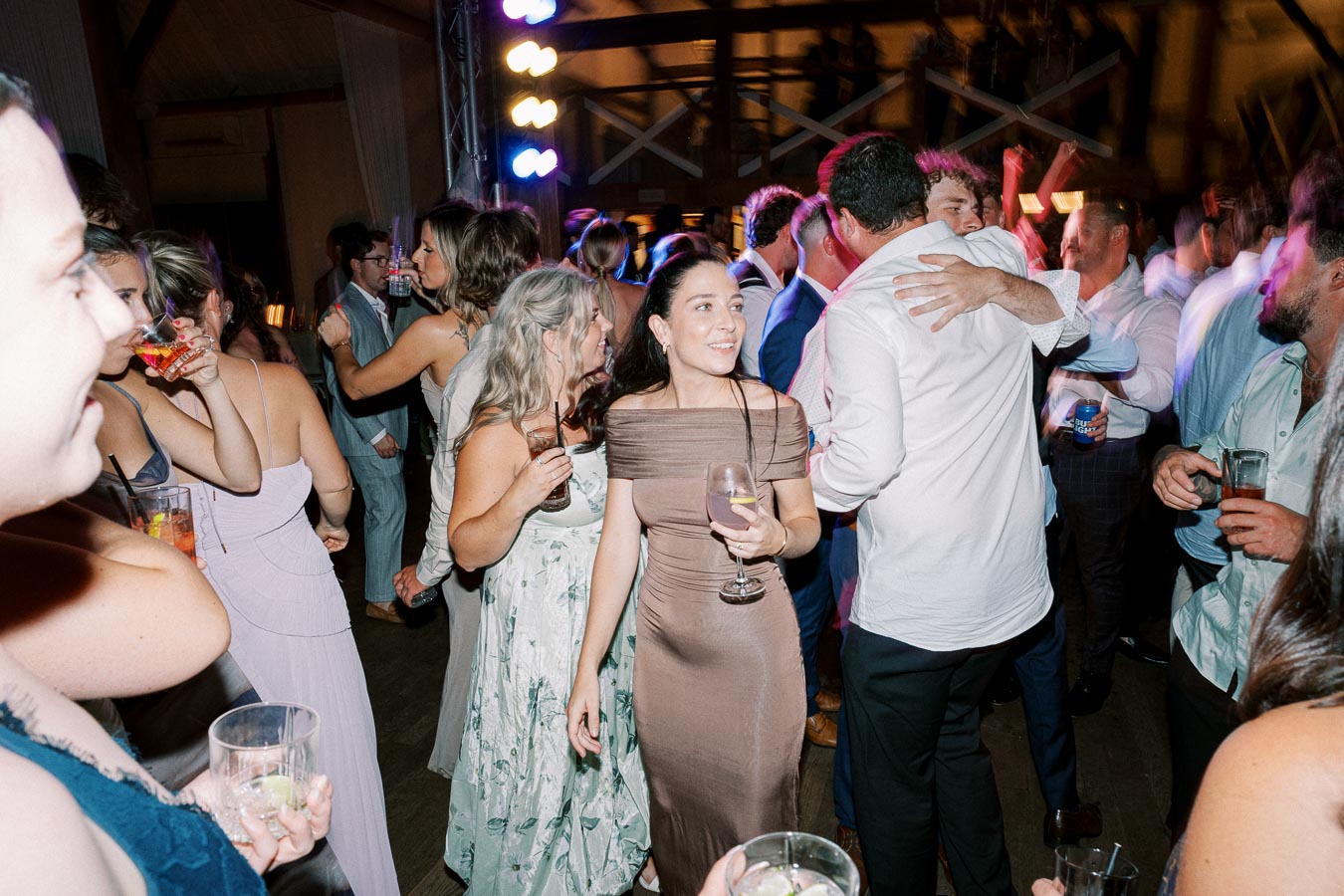 A lively wedding reception with guests dancing and enjoying drinks on the dance floor, illuminated by colorful party lights.