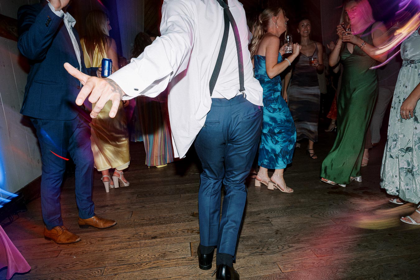 Group of elegantly dressed people dancing at a lively party, wood floor setting, vibrant lighting with motion blur capturing joyful atmosphere.