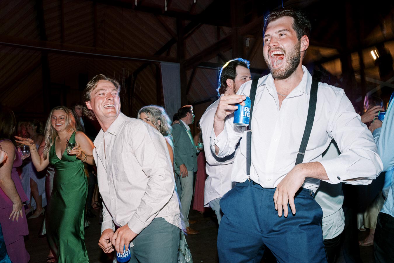Group of friends enjoying a lively dance party in a rustic venue, holding drinks and laughing together under festive lighting.