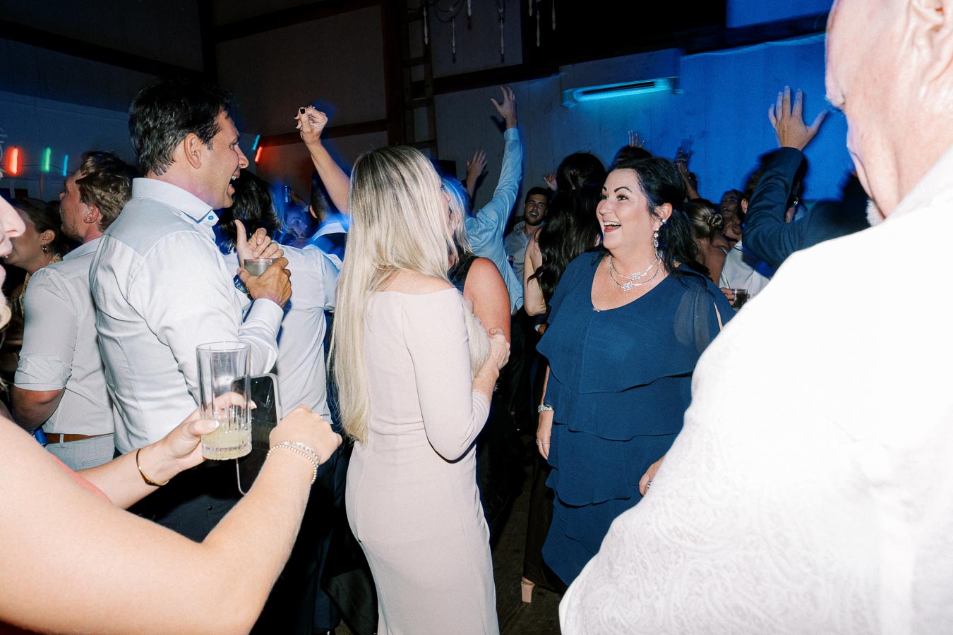 Group of people enjoying a lively party with vibrant lighting and music, featuring guests dancing and socializing in an indoor venue.
