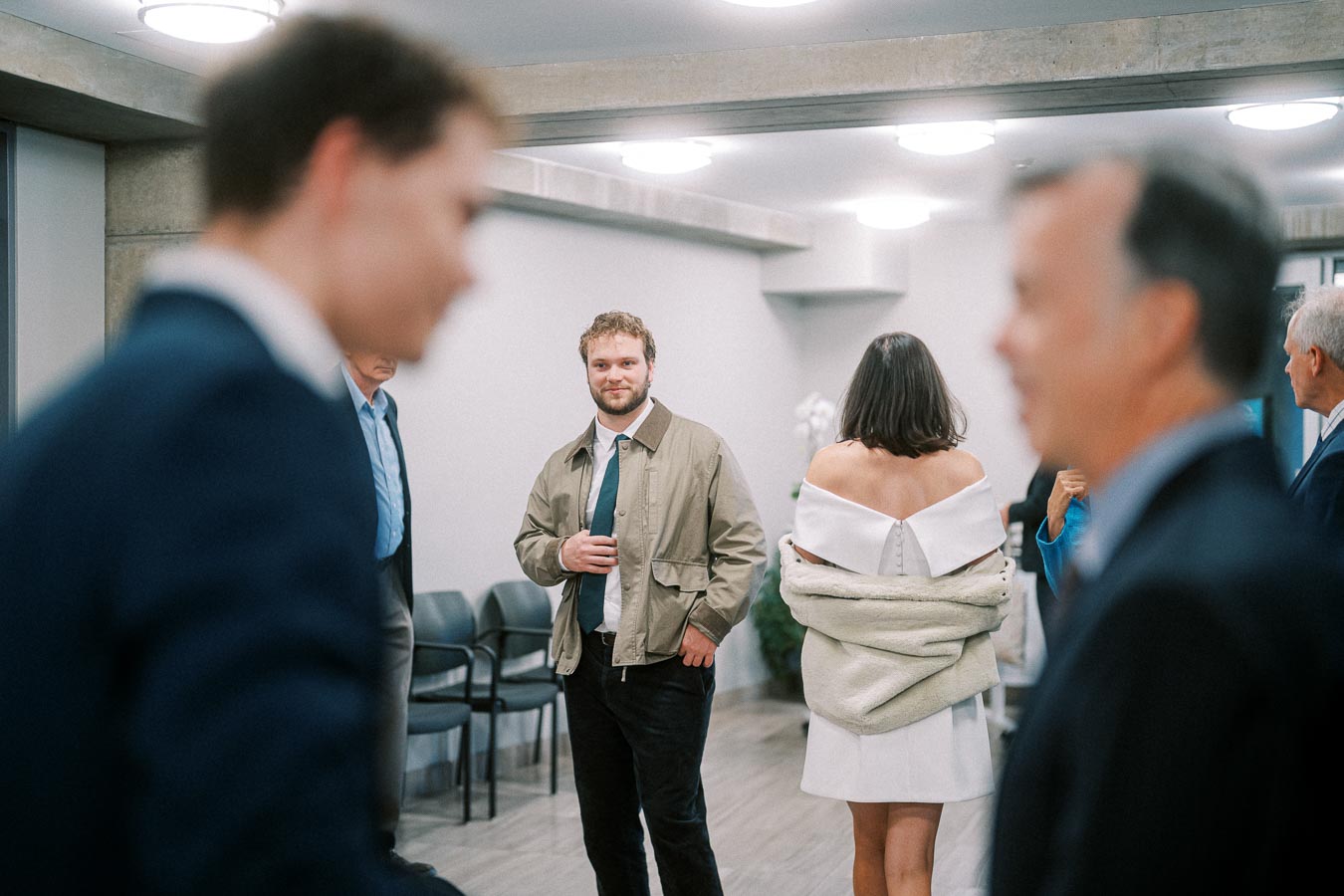 A group of people in formal attire engaged in a conversation at an indoor social event with soft lighting and modern decor.