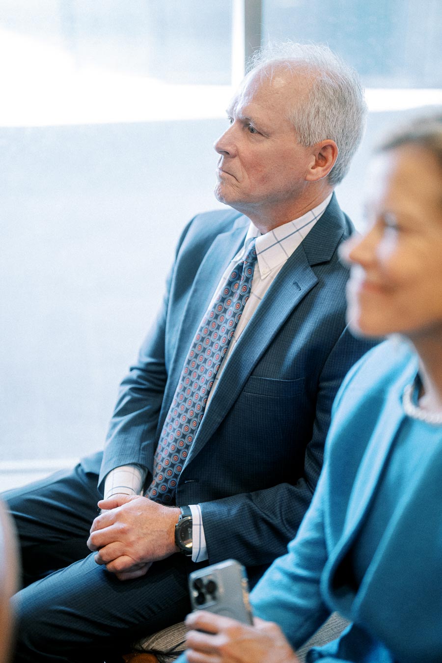 A focused businessman in a suit sits at a professional event, listening attentively.
