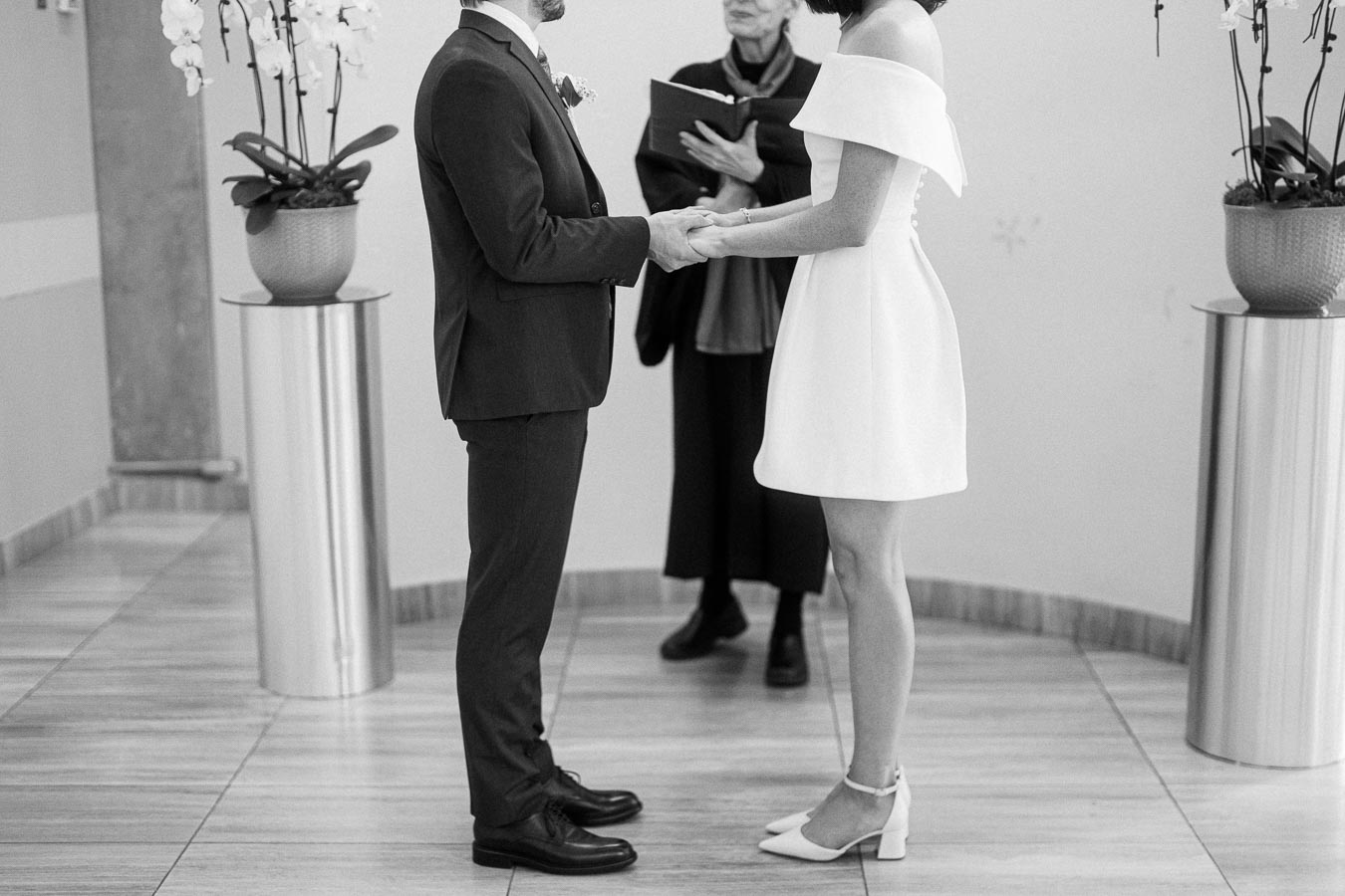 A couple exchanging vows in an intimate indoor wedding ceremony, featuring elegant decor with white orchids and a modern setting.