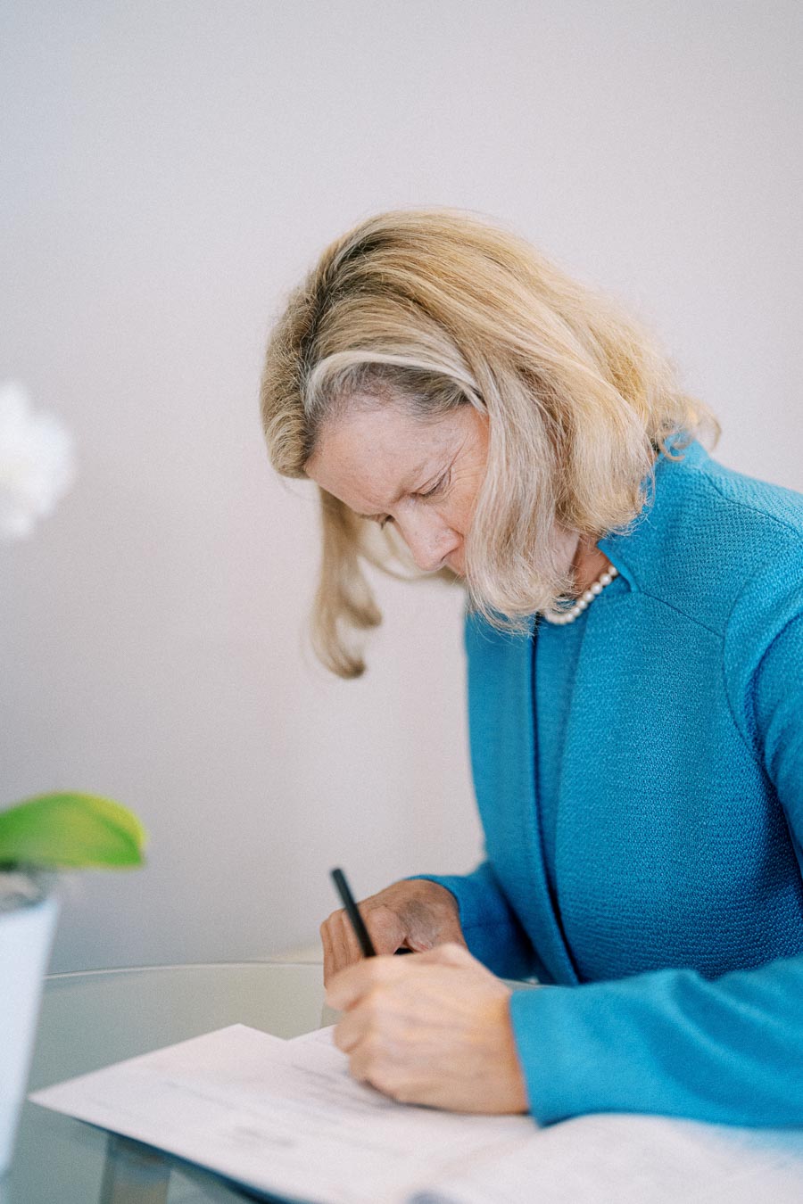 A woman in a blue sweater focusing intently while writing with a pen at a desk, highlighting concentration and productivity in an office setting.