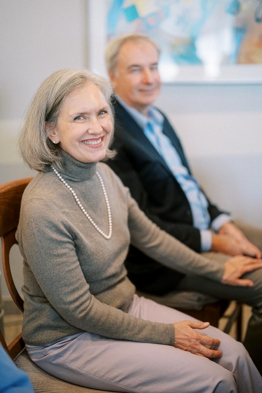 Elderly woman smiling at an event, seated next to a man in a suit, highlighting joyful interaction and community engagement.