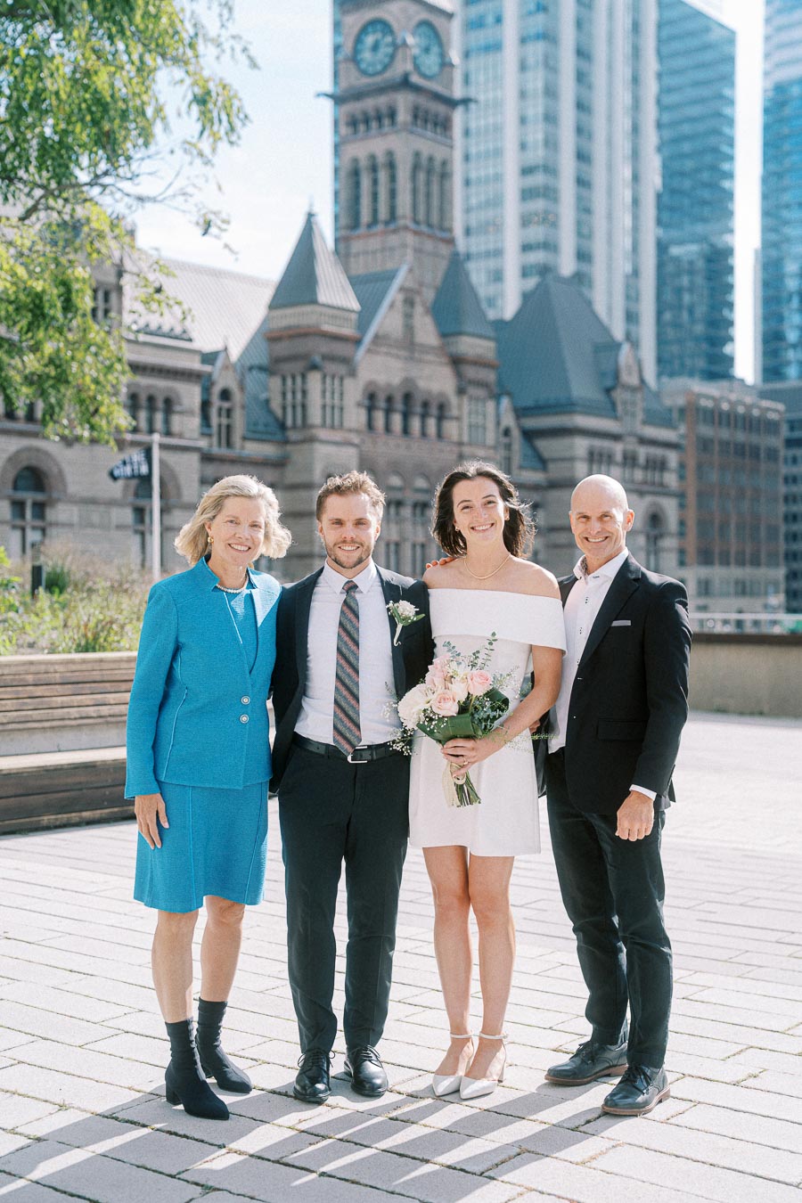 Wedding couple posing with guests in front of an iconic historic building and modern skyscrapers, capturing a blend of tradition and urban elegance.