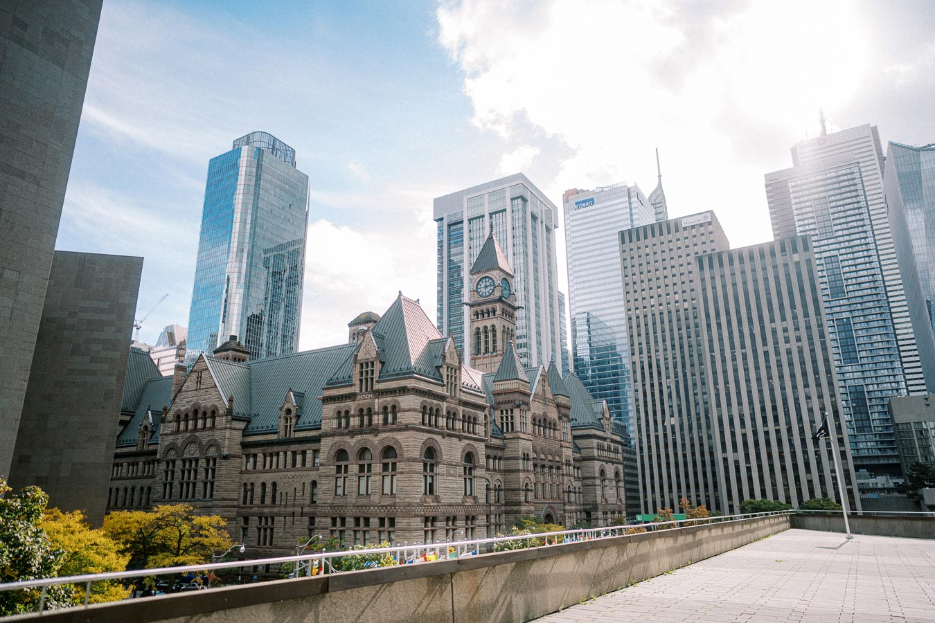 Historical building with a clock tower, surrounded by modern skyscrapers under a partly cloudy sky, showcasing architectural contrast in an urban cityscape.