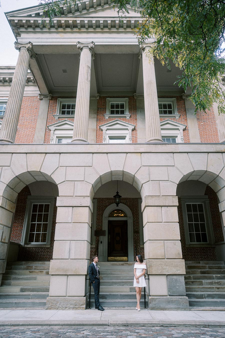 Historic building with tall columns and arched doorways, featuring a couple dressed formally standing on stone steps.