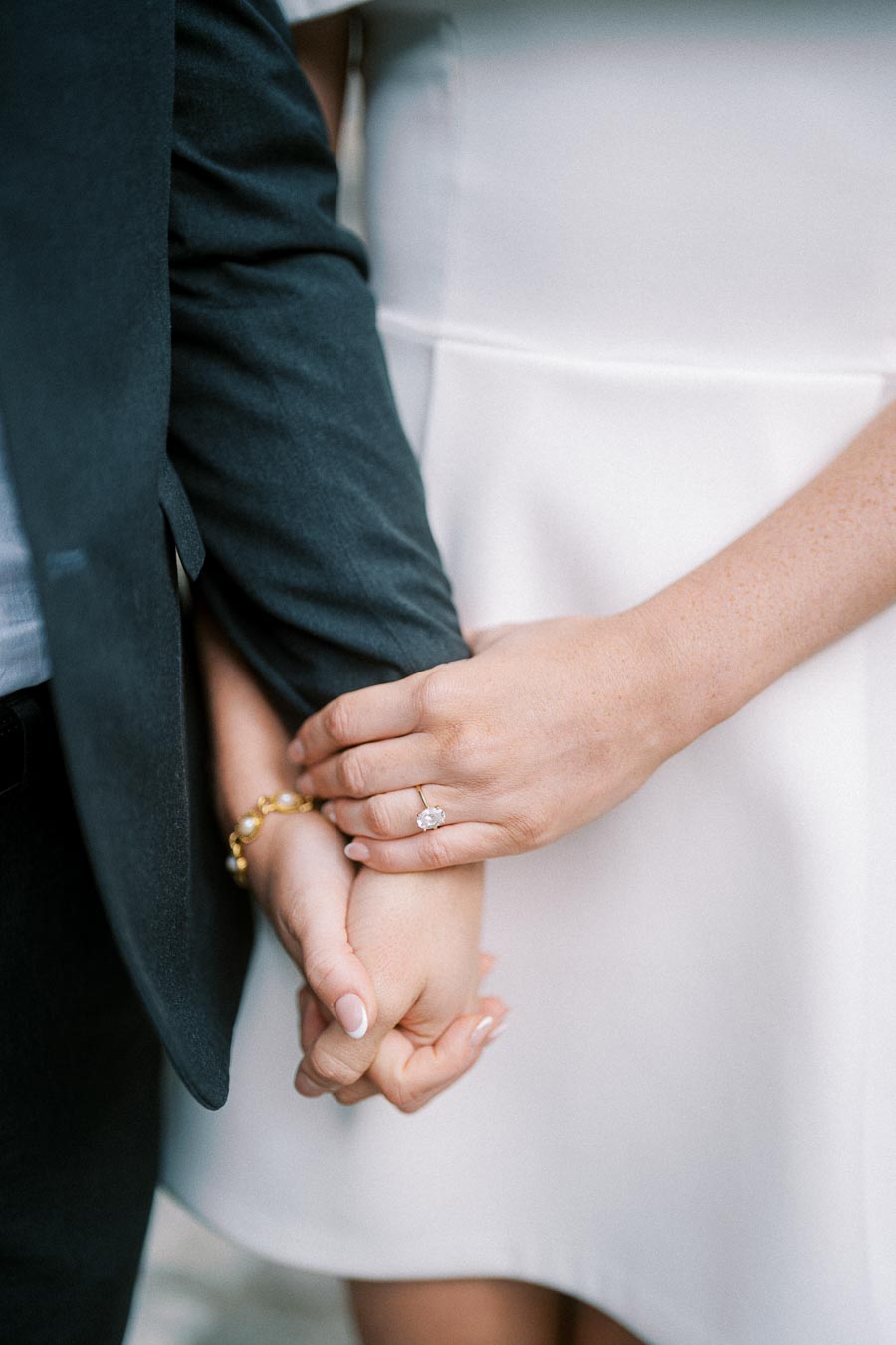 Close-up of a couple holding hands, with a focus on the woman's engagement ring, symbolizing love and commitment.