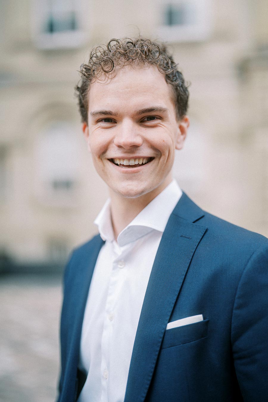 A professional young man in a blue suit smiling confidently outdoors, conveying success and approachability in a business setting.