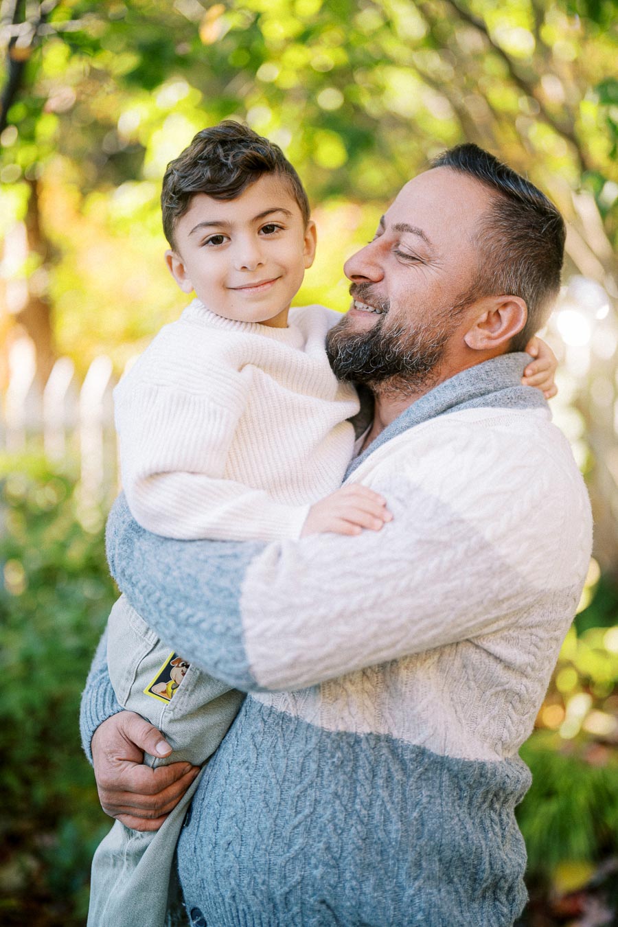 Father and young son enjoying a joyful moment outdoors, surrounded by lush greenery and soft sunlight.