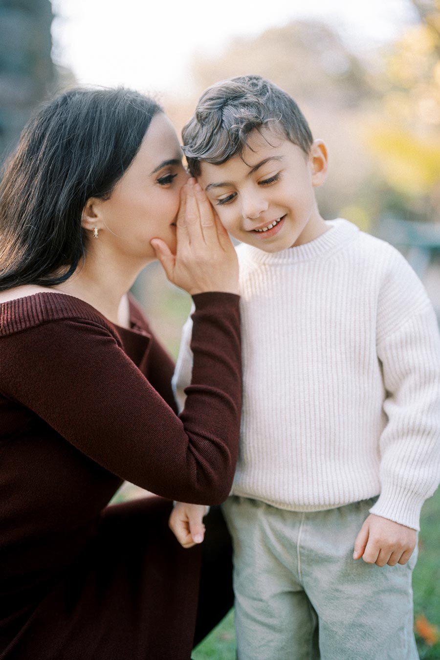 Mother whispering to her smiling son in an outdoor setting.