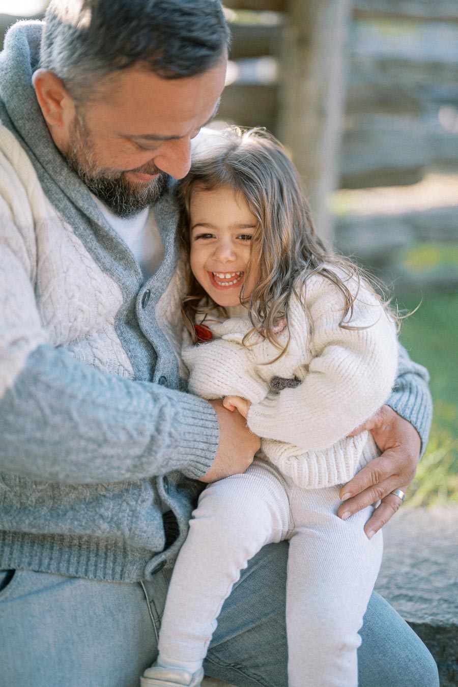Father and daughter sharing a happy moment together outdoors, both wearing cozy sweaters and smiling warmly.