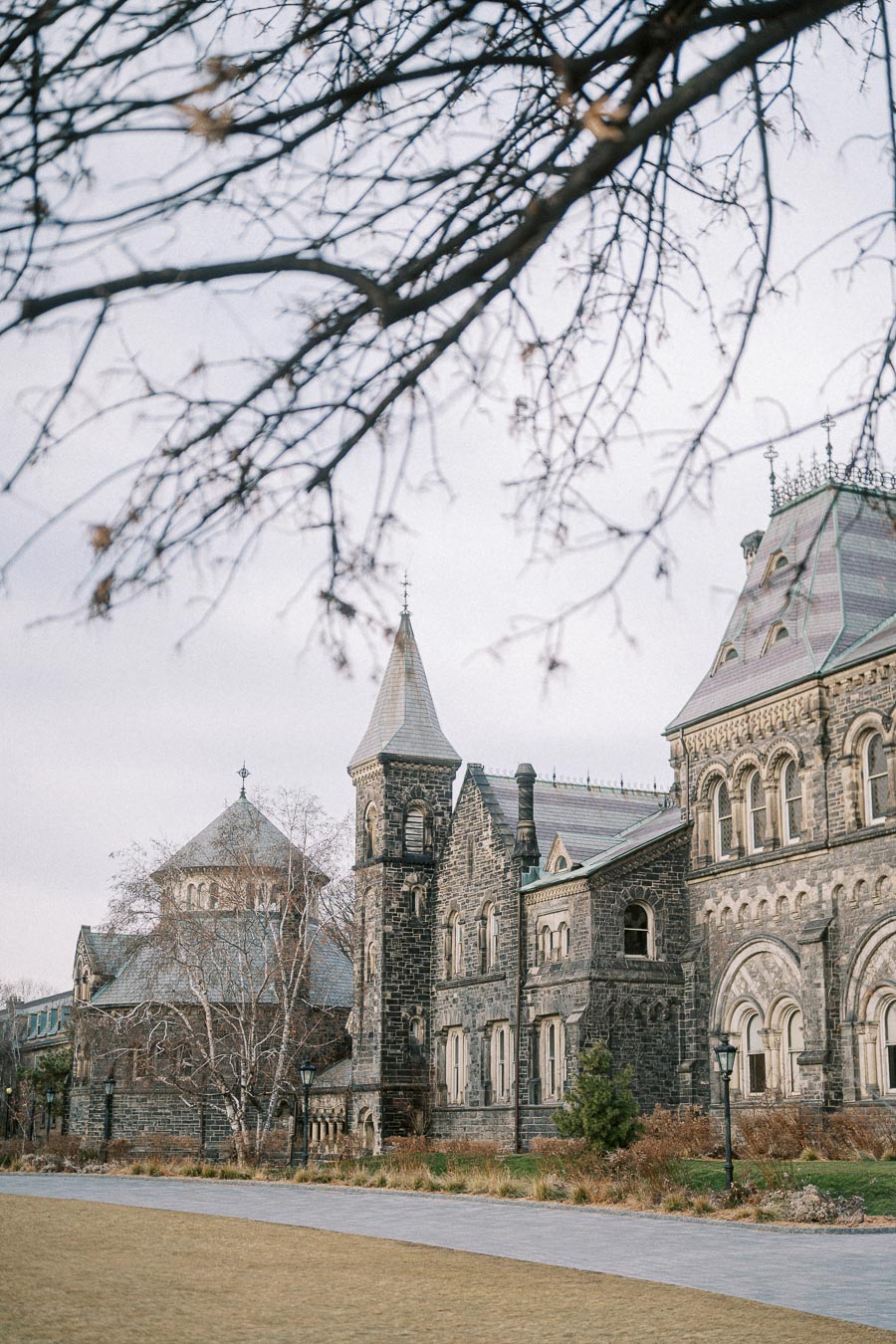 Historic stone building with ornate architecture, featuring tall spires and arched windows, set against a winter sky with bare tree branches in the foreground.